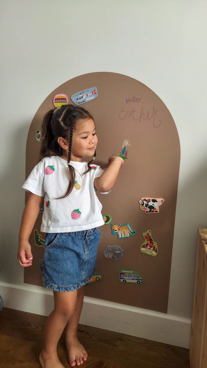 Girl decorating a brown magnetic board and chalkboard with animal magnets and chalk drawings.
