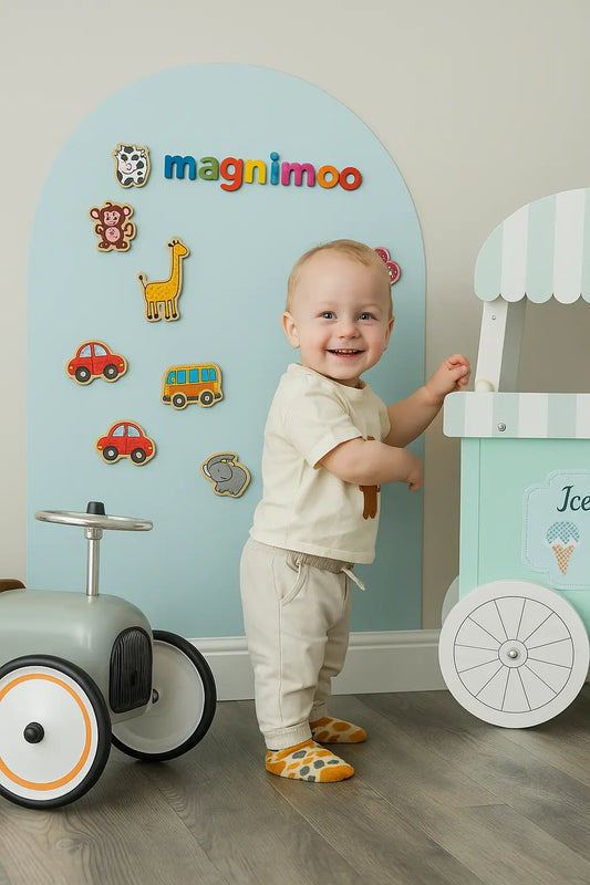 Happy toddler playing beside a ride-on toy with Magnimoo magnet board in Blue Dream arch design