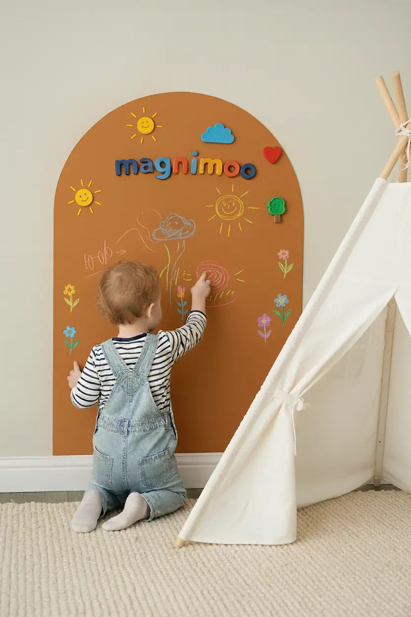 Child drawing on an amber magnetic board and chalkboard with colorful magnets and chalk designs.